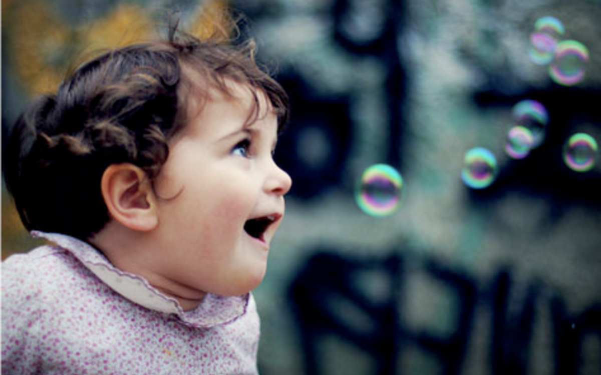 Une petite fille de 3 ans environ aux cheveux bouclés s'émerveille devant des bulles de savon