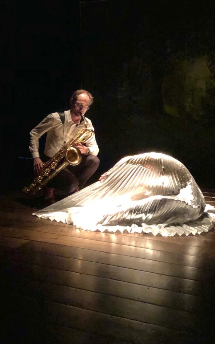 saxophoniste et danseuse au sol dont on ne voit que la longue jupe blanche et plissée