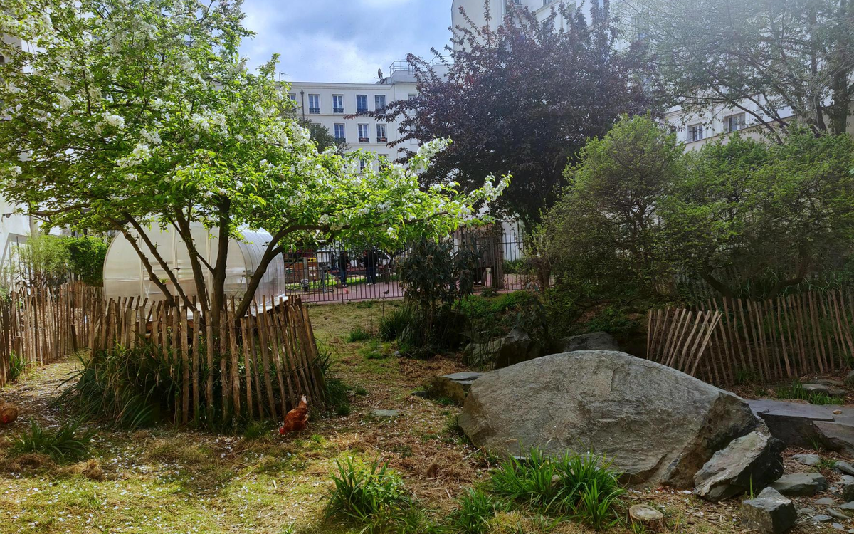 Au premier plan, des arbres et des poules. En arrière plan, une serre.