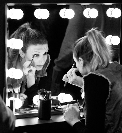 Photo en noir et blanc d'une comédienne qui se maquille avant de tourner un film chez Make It Clap Studio