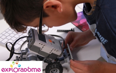 Un enfant en train de monter son robot fait de Légo à l'Exploradôme.