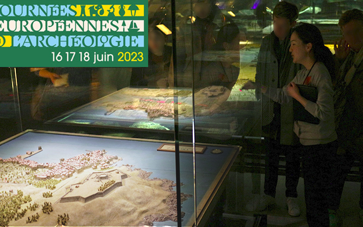 Dans la pénombre du musée, une médiatrice présente à des visiteurs la maquette de Saint-Tropez.