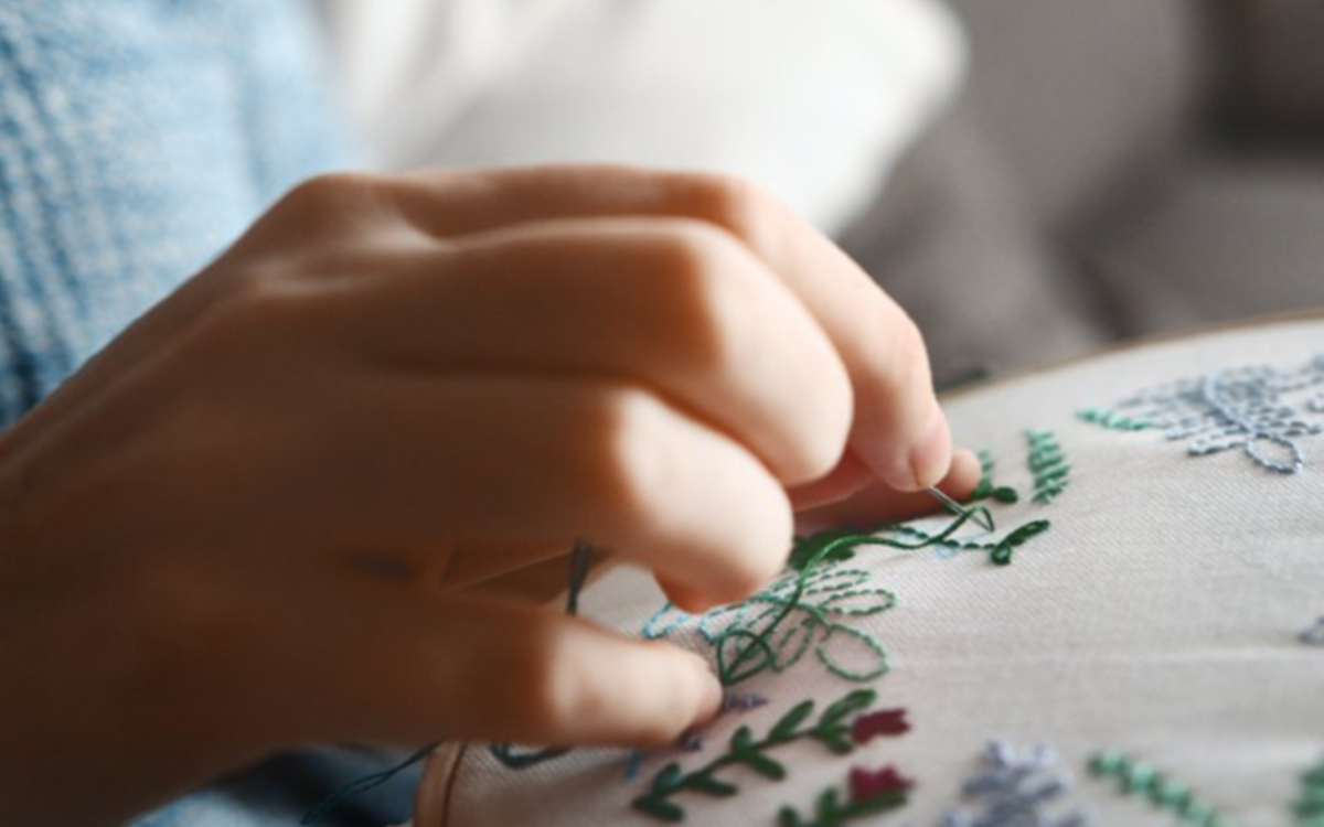 Atelier broderie. une main qui brode un tissu. Des fleurs réalisées.