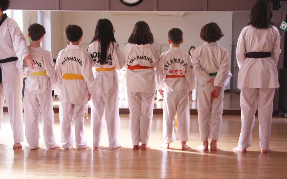 Des enfants de dos, en lignes, dans une salle de sport, avec des tenues de taekwondo