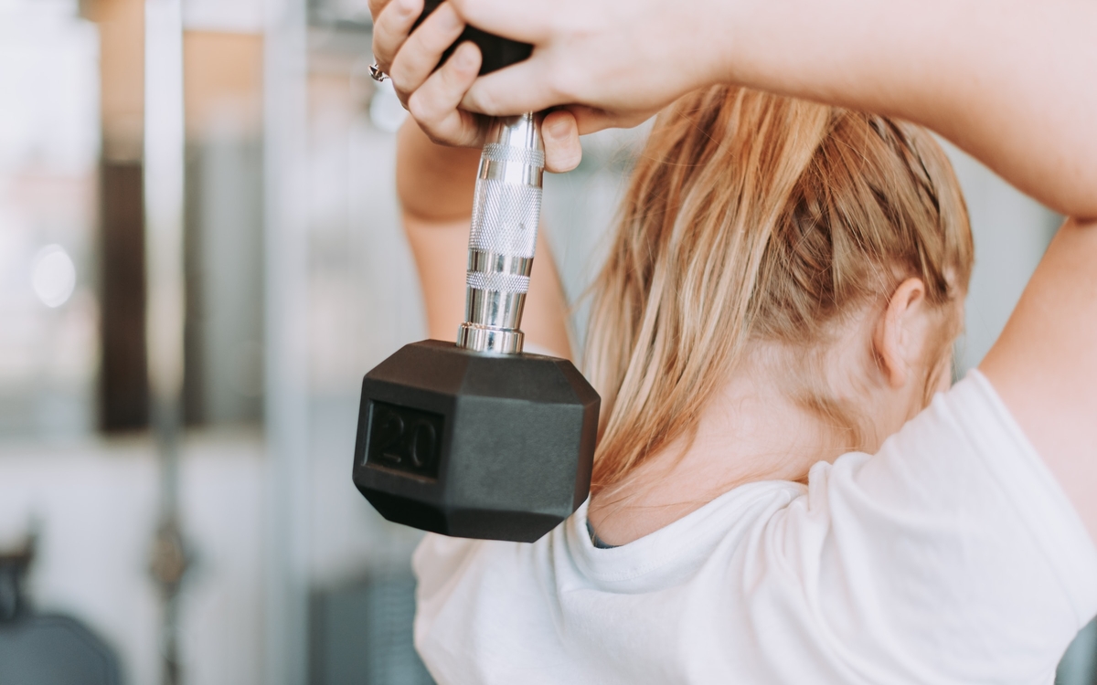 Femme de dos, tenant un poids à deux mains derrière sa tête