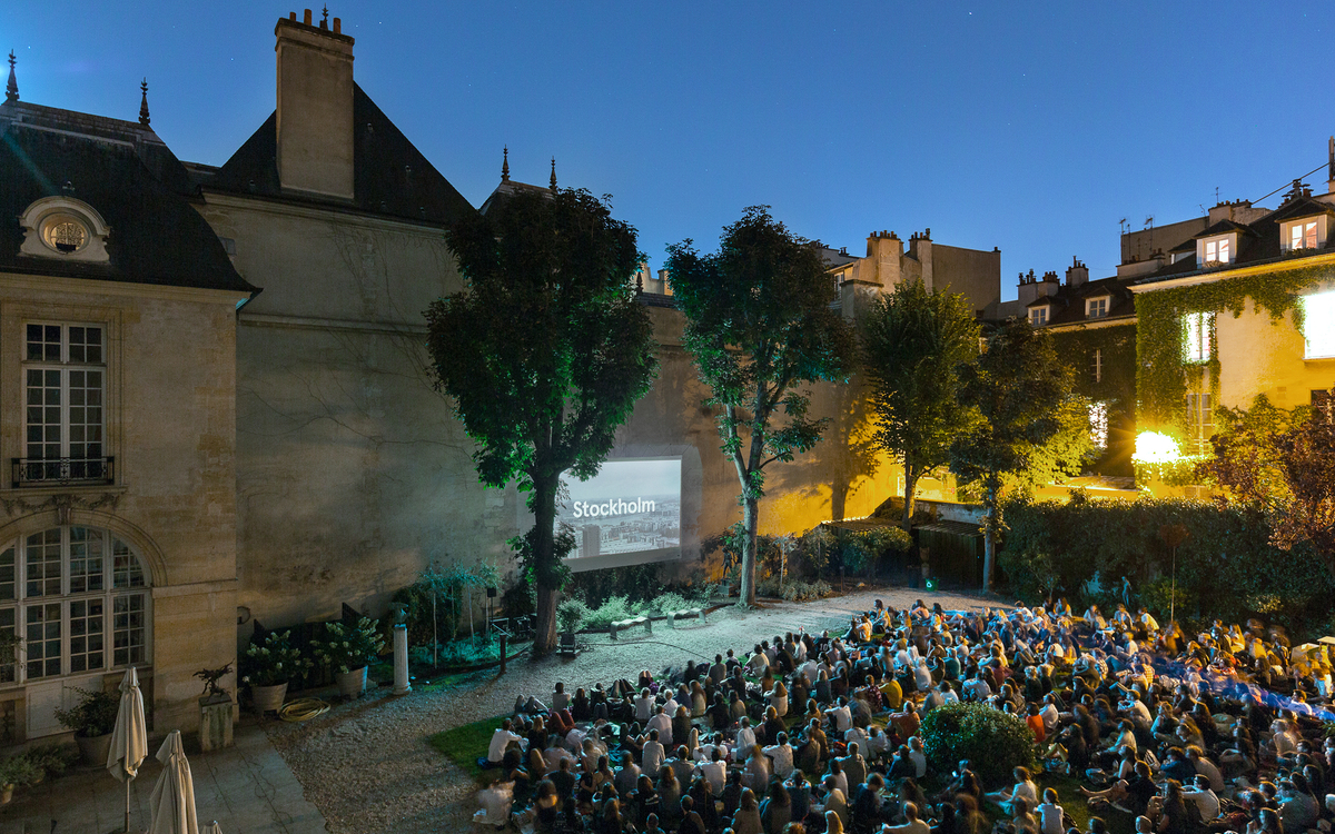 Foule de spectateurs assis dans le jardin de l'Institut suédois, face à l'écran géant.