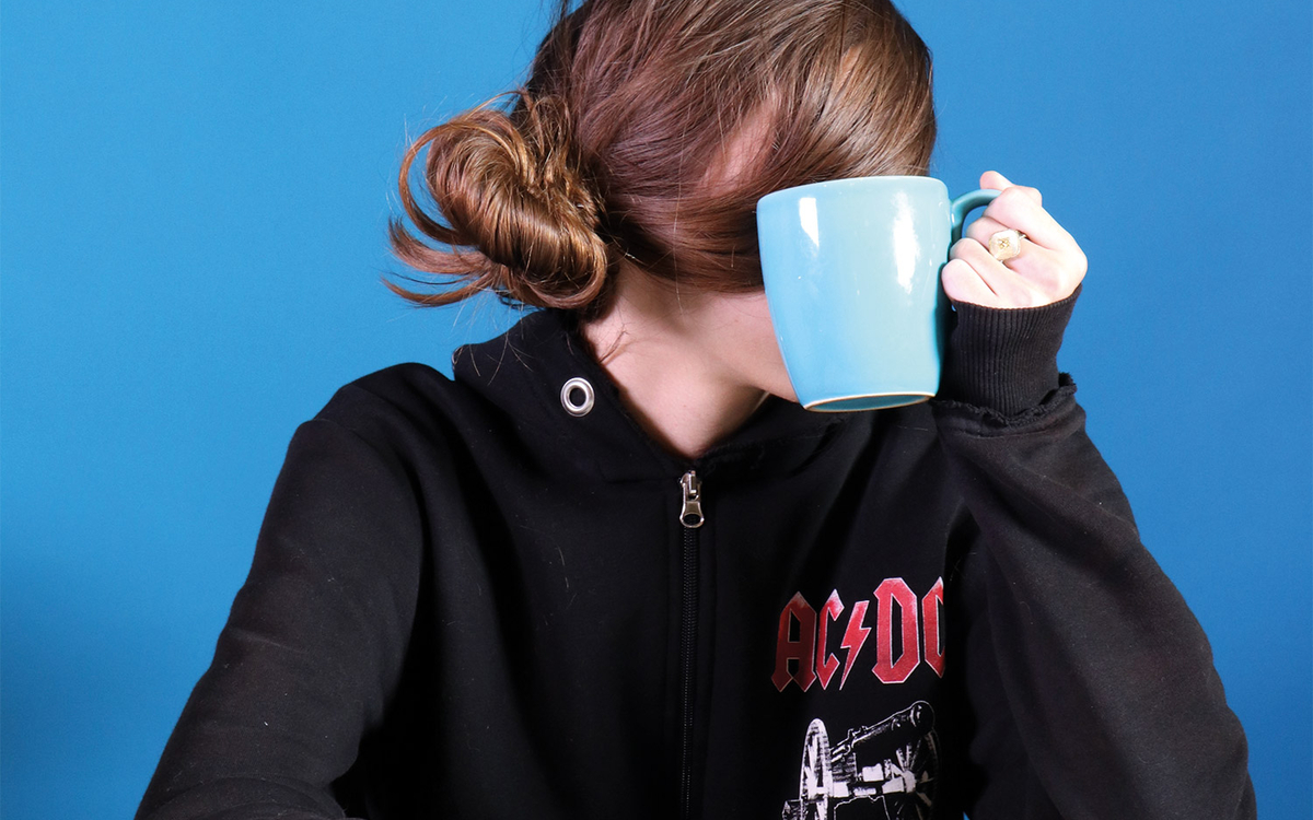 Portrait d'adolescente pull noir à capuche, avec le logo d'ACDC qui se cache derrière une tasse