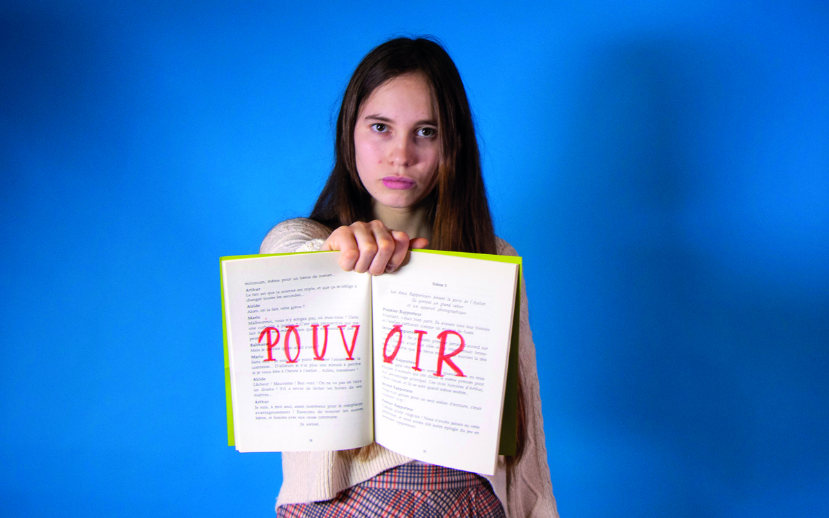 Portrait d'une jeune fille à l'air déterminé qui nous présente un livre ouvert où est inscrit au feutre rouge le mot "pouvoir"