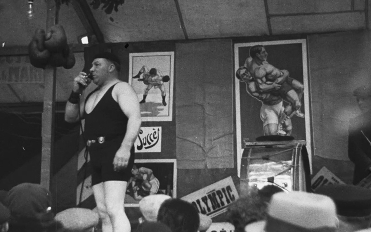 Parade devant une baraque foraine d'un lutteur présentant son spectacle