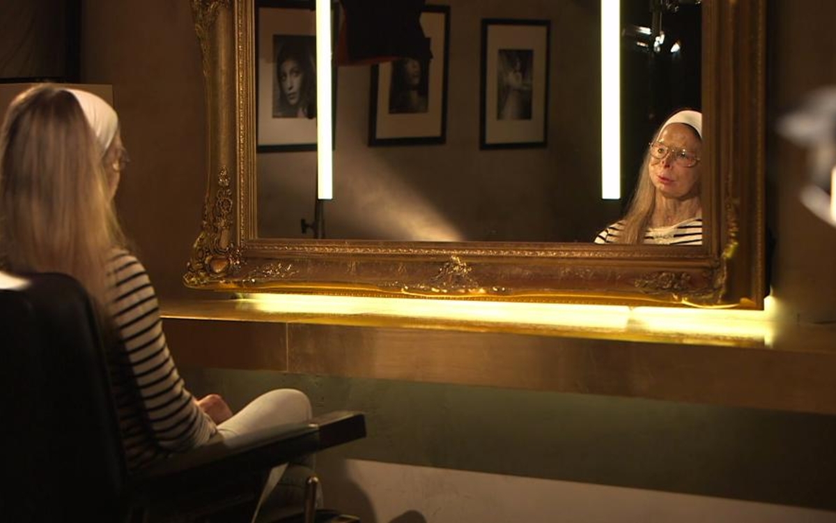 Femme de dos regardant son visage flétri dans un miroir éclairé