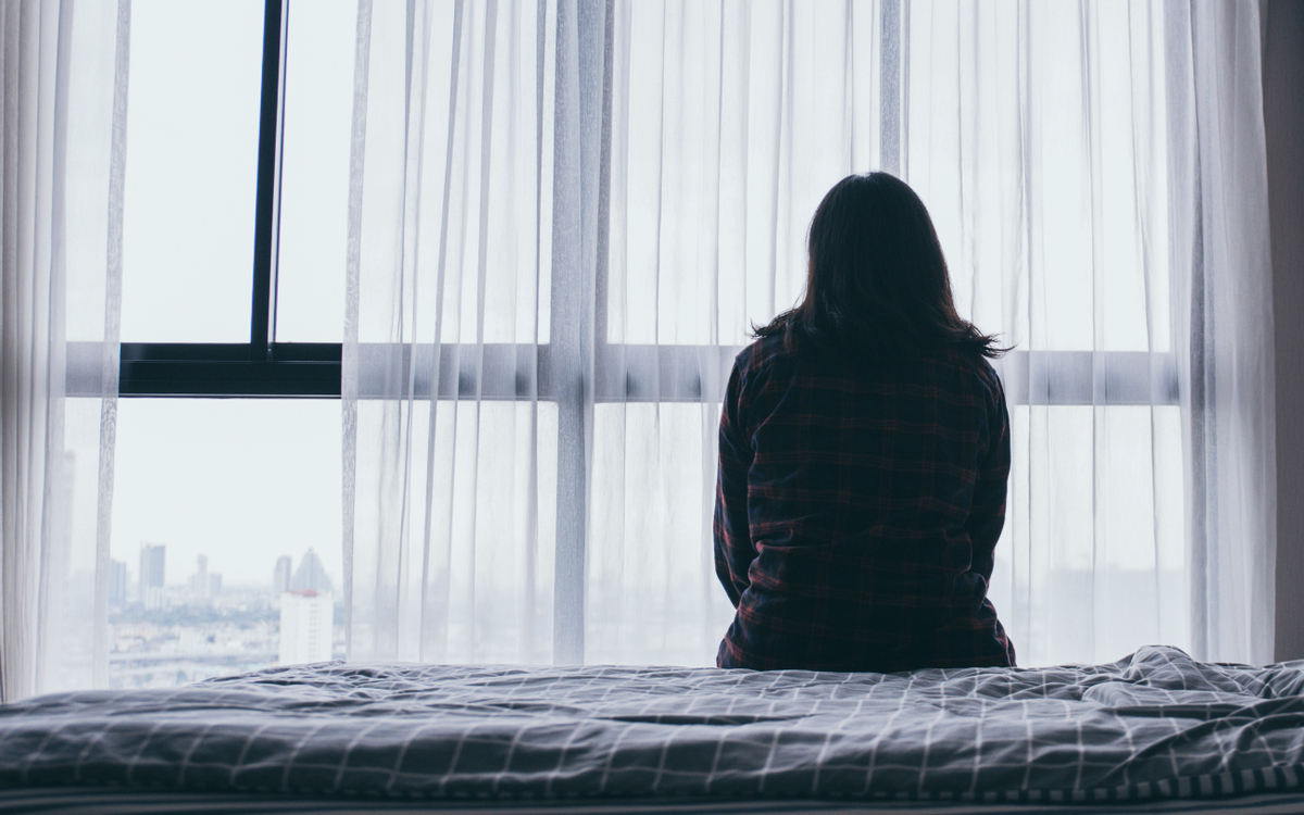 Femme triste, seule sur un lit, regardant vers la fenêtre