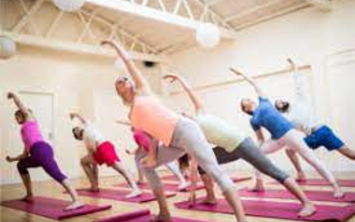 Personnes debout sur un tapis de sport rose qui se penchent vers la gauche avec leur mains et leur bras droit tendu au dessus de leur tète. 