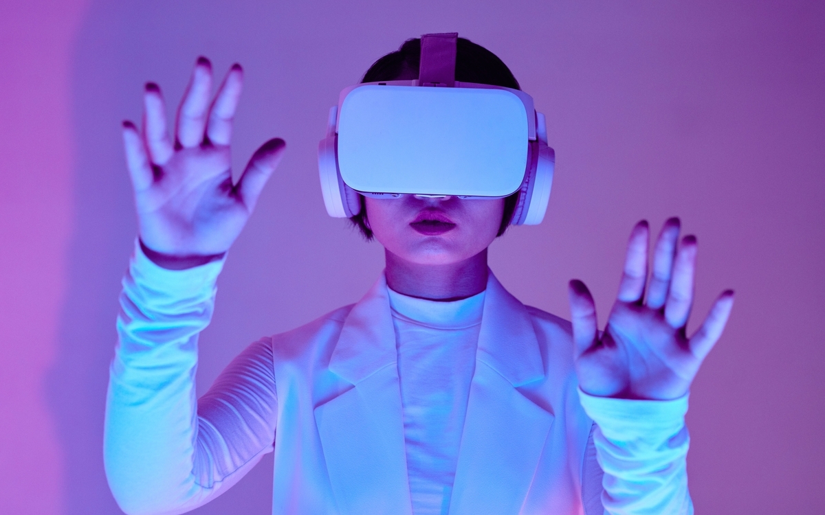 Personne portant un casque Vr sur la tête levant les main devant elle semblant toucher un mur invisible lui faisant face.