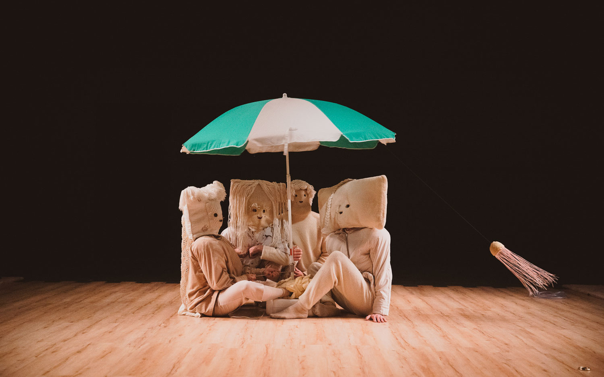 Personnages masqués regroupés sous un parasol, sur scène