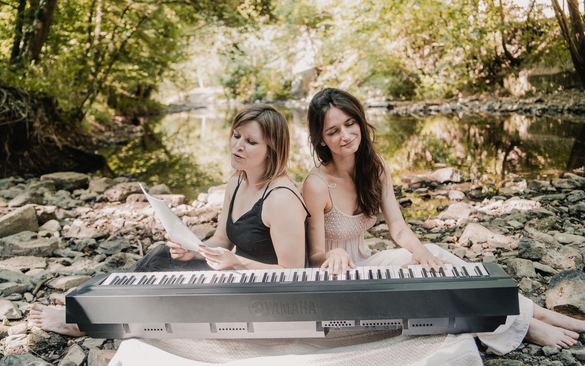 Deux femmes jouent du piano et chantent au bord d'un ruisseau.