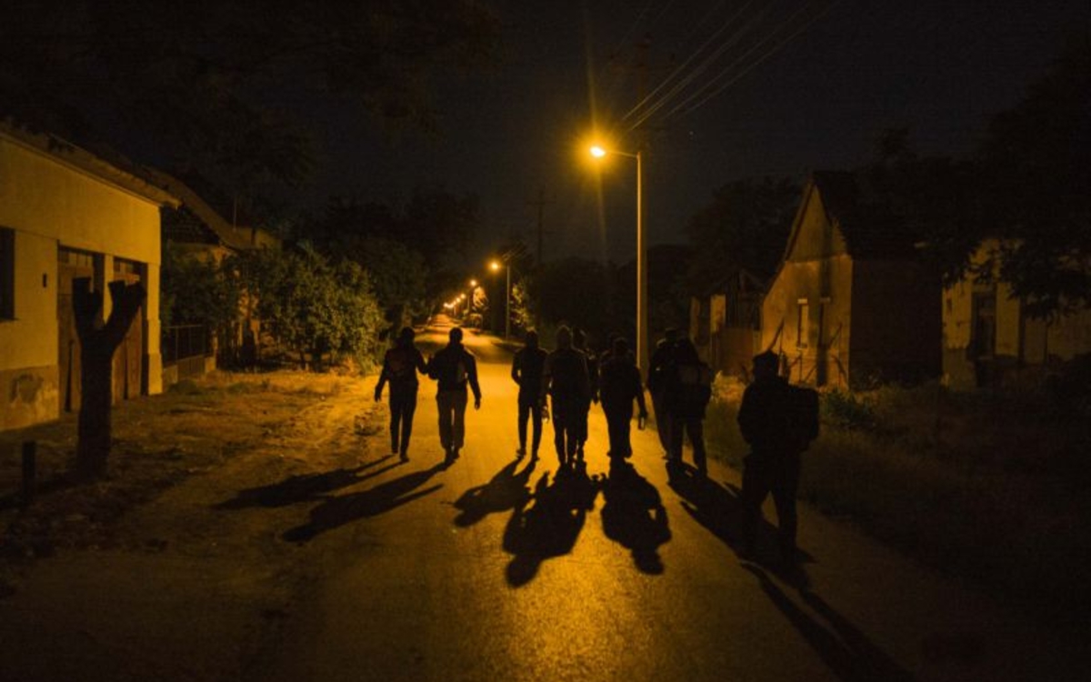 Dans la nuit, un groupe de personnes avancent dans une rue éclairée 