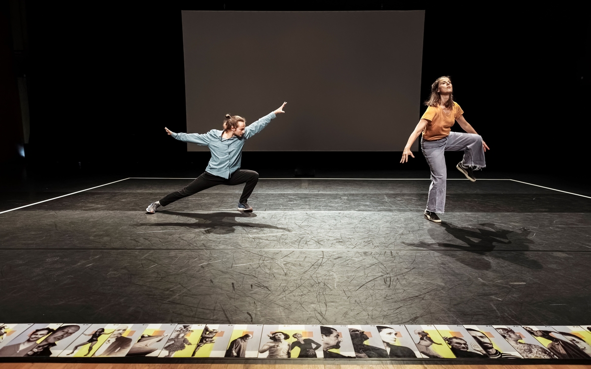 Deux danseurs sur un plateau noir, avec des photos aligné au sol au premier plan