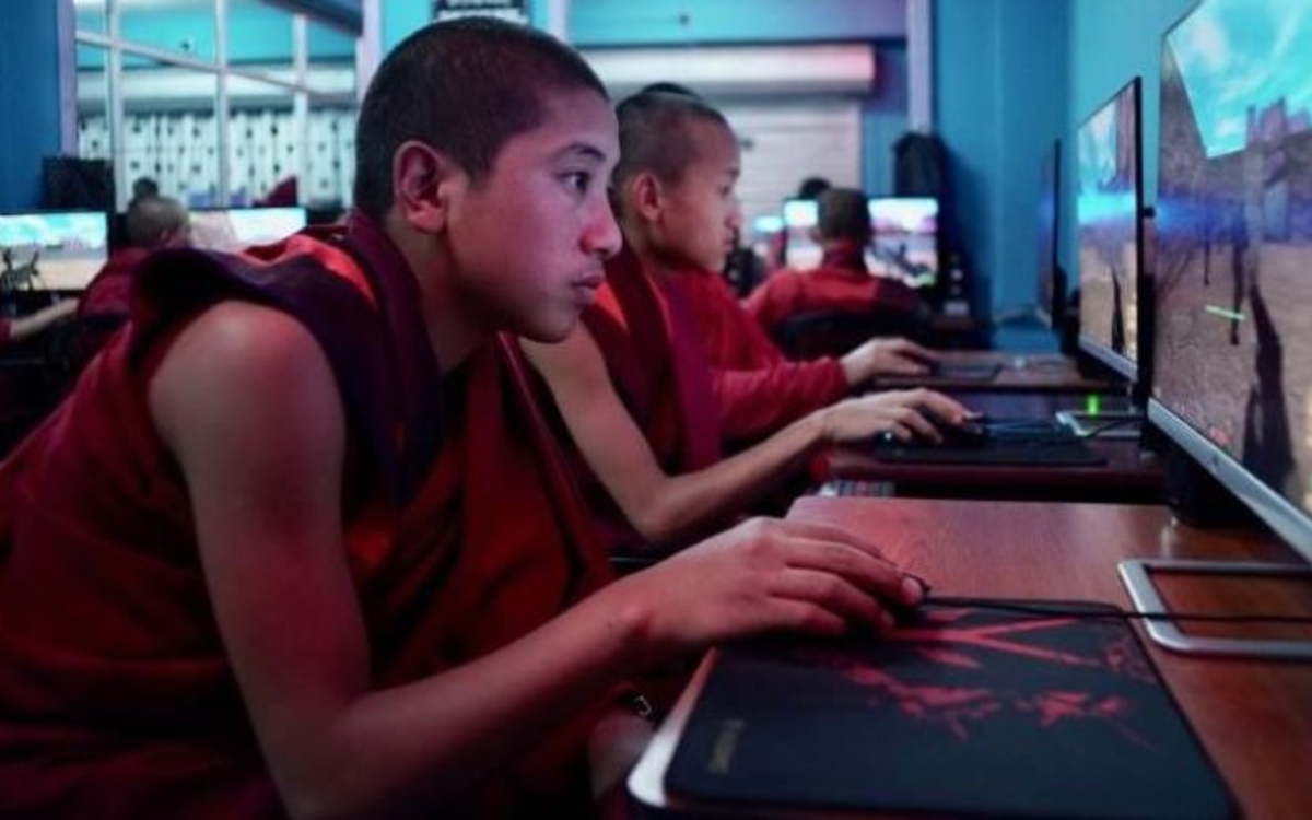 Des moines bouddhistes revêtus de leur tenue traditionnel devant des écrans d'ordinateurs