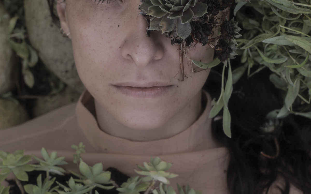Visage de l'artiste entourée de végétaux. Du feuillage recouvre son oeil gauche.