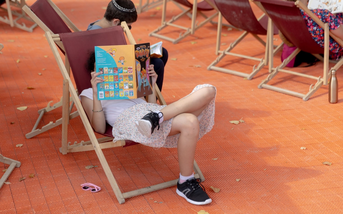 Jeune fille lisant un livre sur un transat, en plein air. 