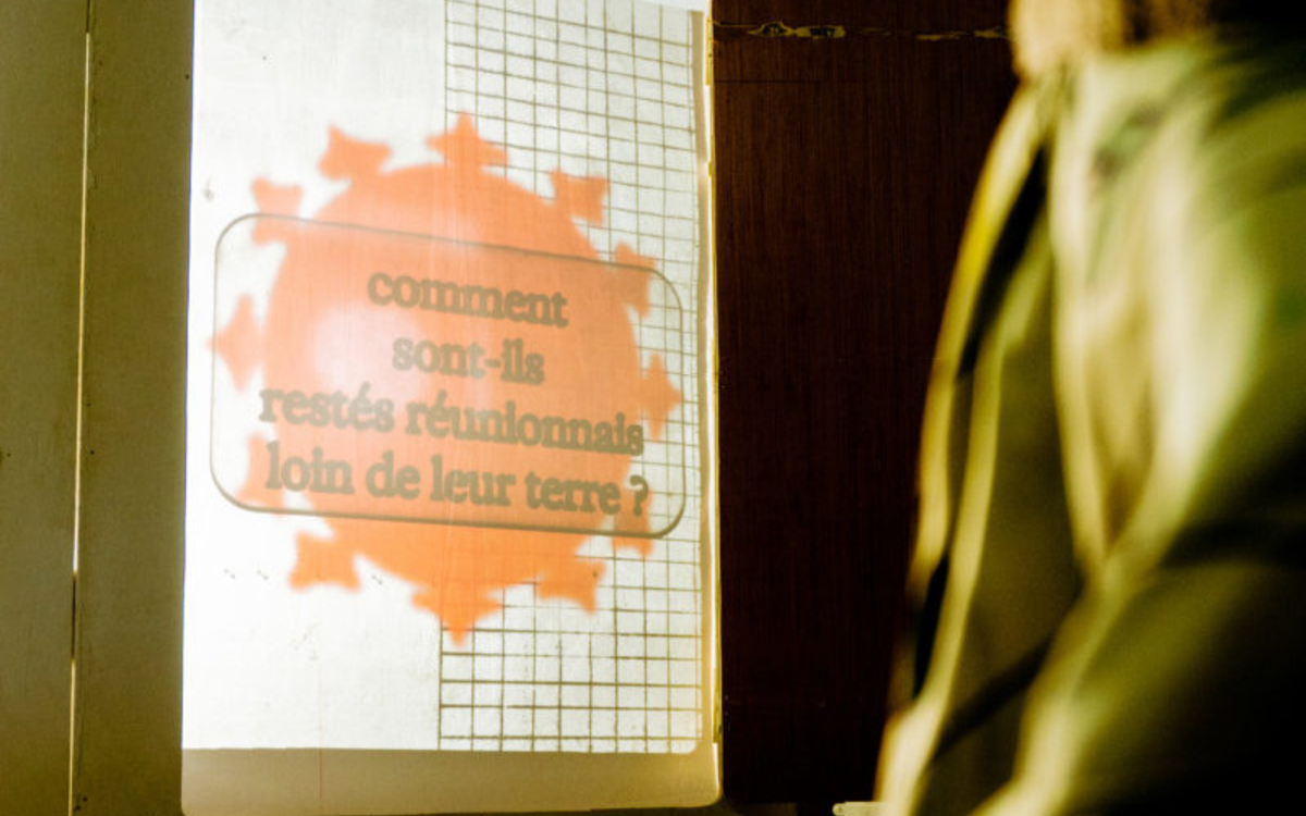 L'image est un extrait de la performance Racontaz aux soleyls, on voit un texte projeté sur un mur qui dir "comment sont-ils restés réunionnais loin de leur terre ?". Sous ce texte projeté on peut voir le numéro 72. 