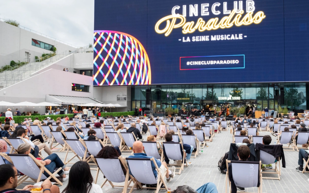 Des gens allongés sur des transats visionnent un film sur grand écran en plein air