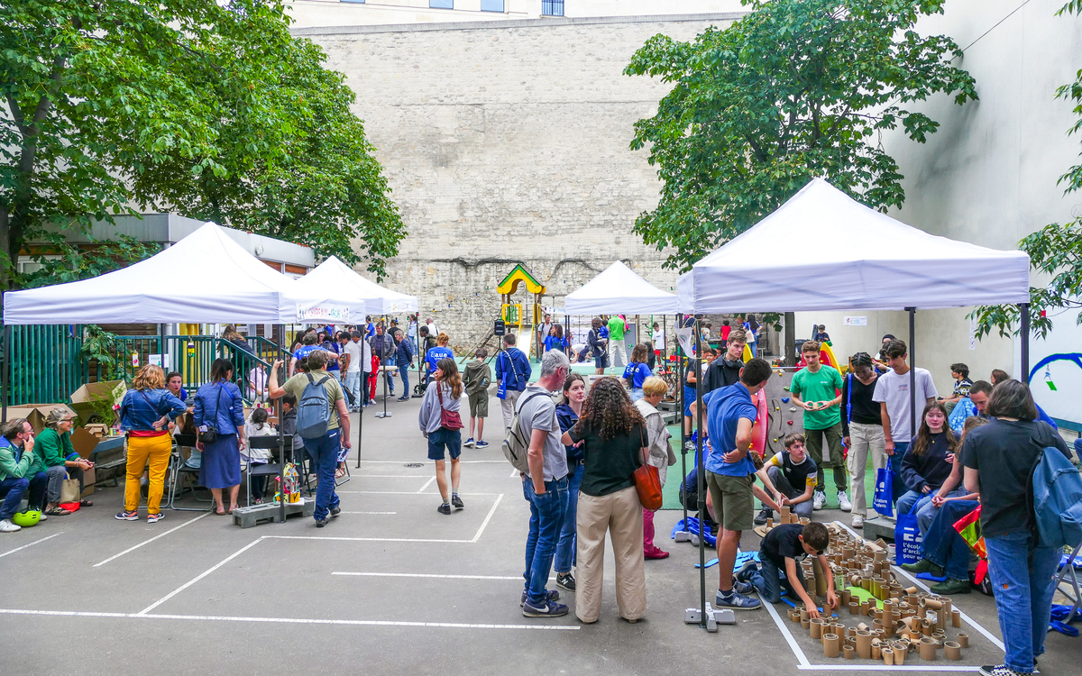 Fête de l'école d'architecture pour enfants dans une cour d'école, avec des barnums et de nombreuses personnes participant à des activités