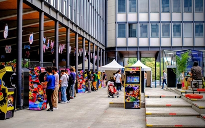 Joueurs profitant des bornes d'arcades à disposition lors du Play Sorbonne Festival 2023. On apperçoit une des tentes des développeurs de jeux indépendant. 