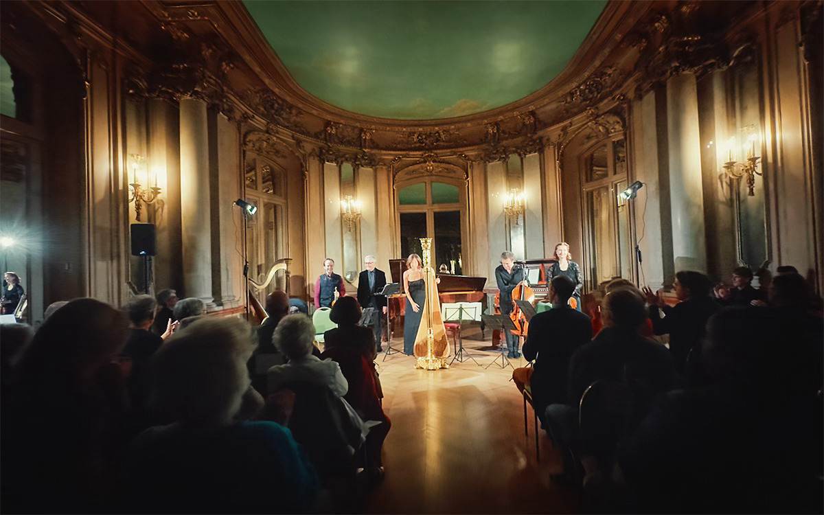 Affiche promotionnelle du Festival Érard, 3e édition, se déroulant les 11, 12 et 13 octobre 2024. L’image montre un concert de musique classique dans une salle élégante avec des musiciens sur scène, notamment une harpiste au centre. Le programme met en avant les compositeurs Fauré, Debussy et le poète Verlaine sous le thème des ‘Fêtes Galantes’. L’affiche est ornée de calligraphie pour le nom du festival, avec des couleurs chaudes et une atmosphère intime.