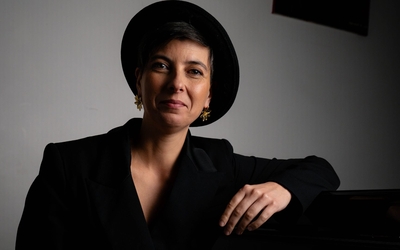 portrait de Noémie Ochoa pianiste compositeur accoudé à son piano à queue. Elle sourit et porte une combinaison noir et un chapeau stetson