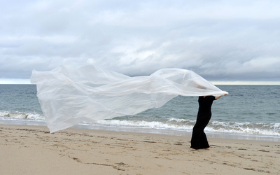 sur une plage l'hiver une femme pieds nus un voile au vent 