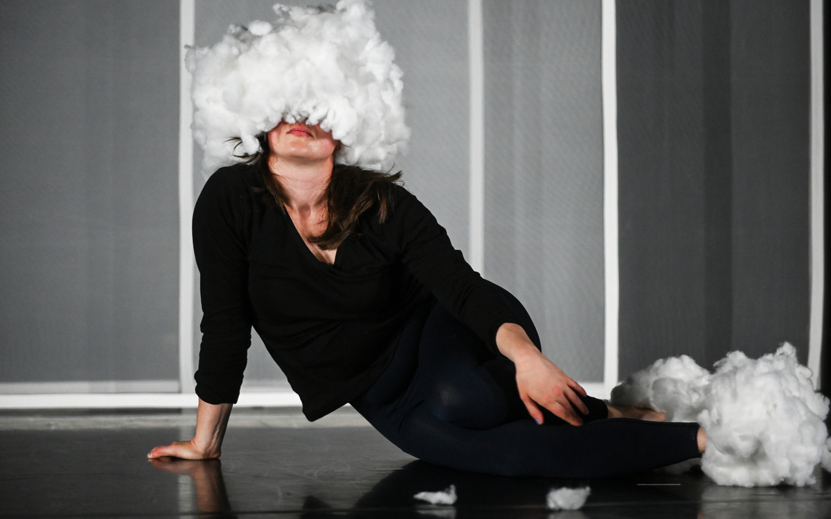 Une femme habillée en noir et assis par terre avec des plumes qui lui couvrent le visage