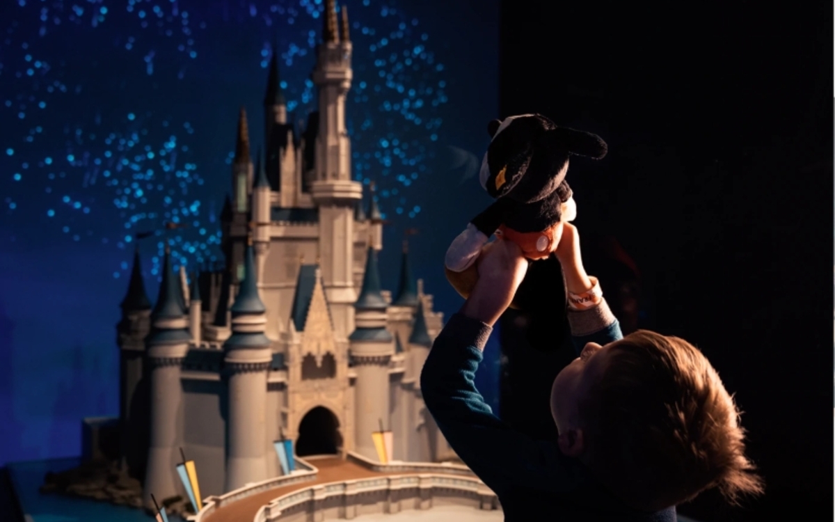 Enfant de dos, tenant une peluche mickey devant la maquette du chapeau Disney