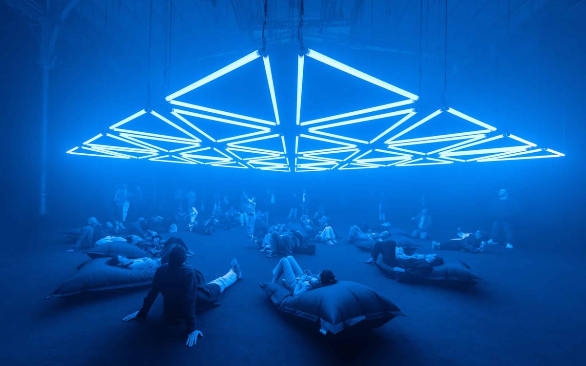Un groupe de personnes assis sur des coussins dans une salle éclairée par des installations lumineuses bleues