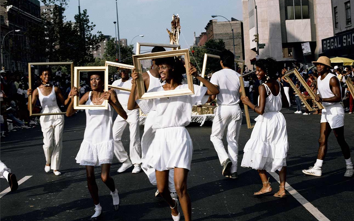 Photographie de Lorraine O'Grady représentant des afro-américains habillés de blanc en train de manifester artistiquement dans les rues, un cadre vide encerclant leurs visages