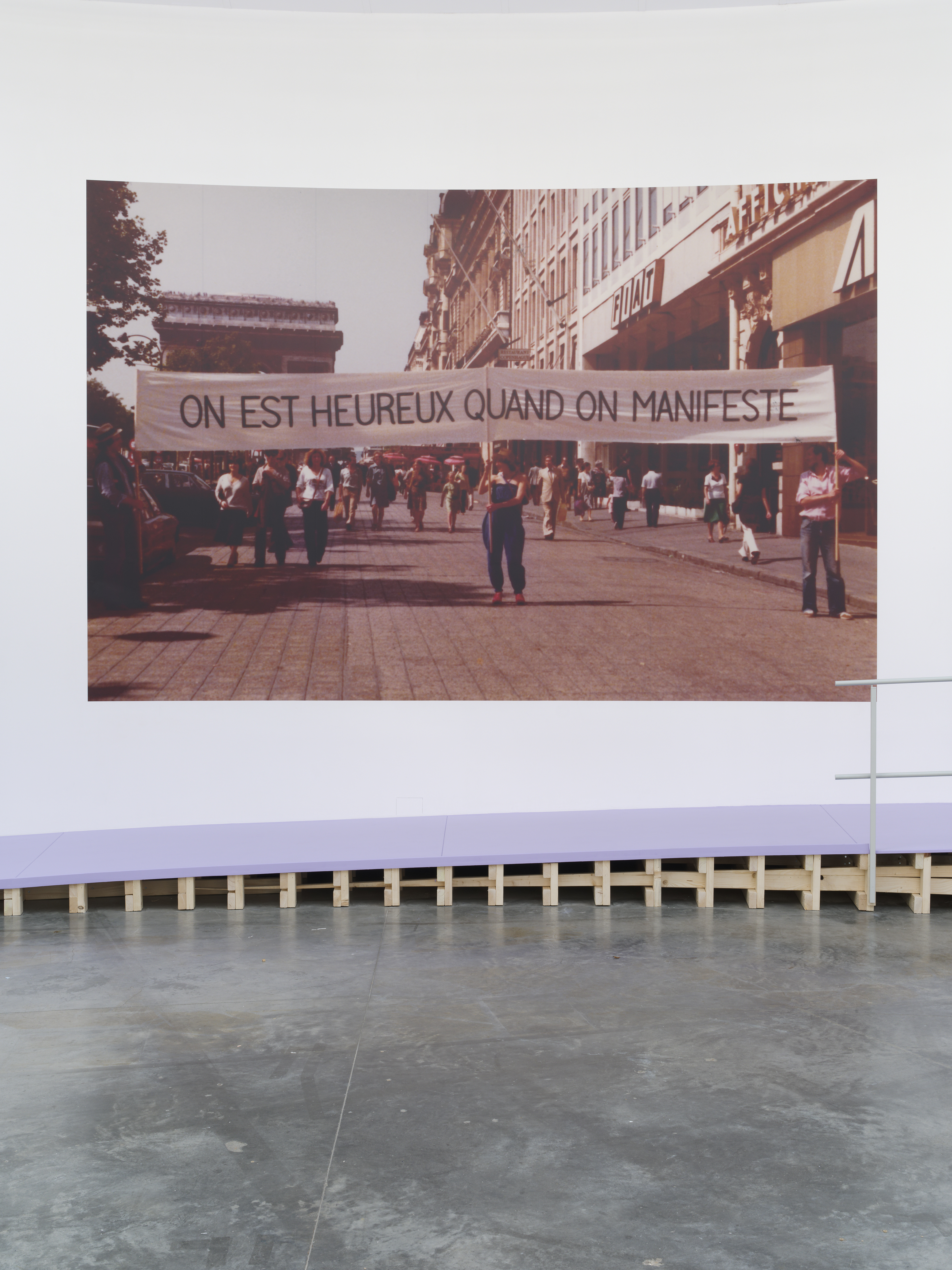 Photographie représentant des personnes marchant dans une rue en tenant une banderole "On est heureux quand on manifeste" 
