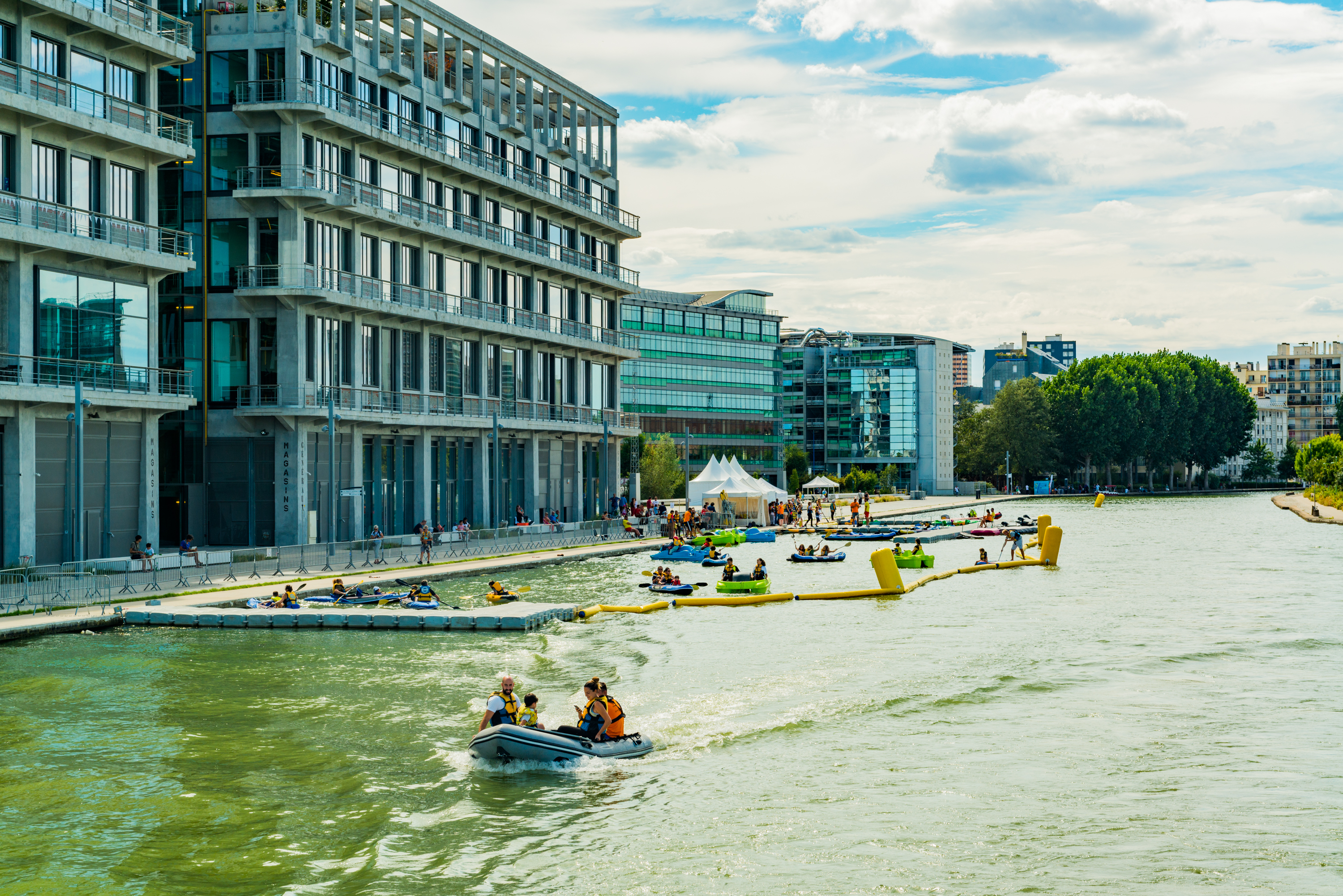 Photo sur le canal de l'Ourcq representant une base nautique avec des individus à bord d'un bateau