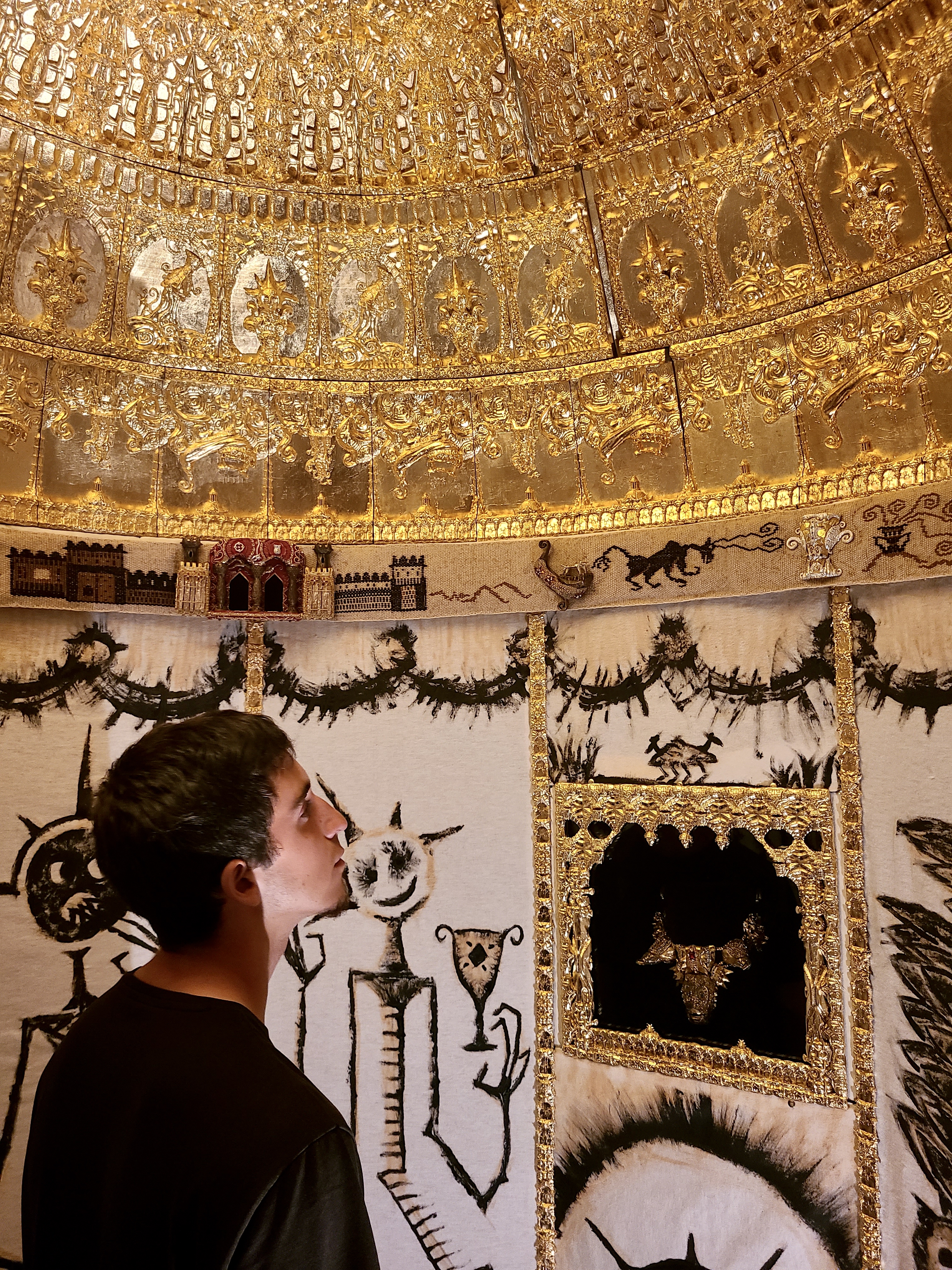 Un homme observe une installation artistique de broderie dorée 