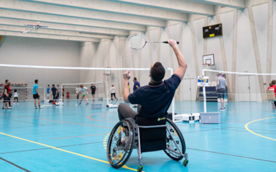 Personne en fauteuil roulant jouant au badminton dans un gymnase.