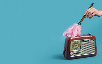 Un vieux radio-transistor, sur fond bleu, avec une main qui tient un plumeau rose