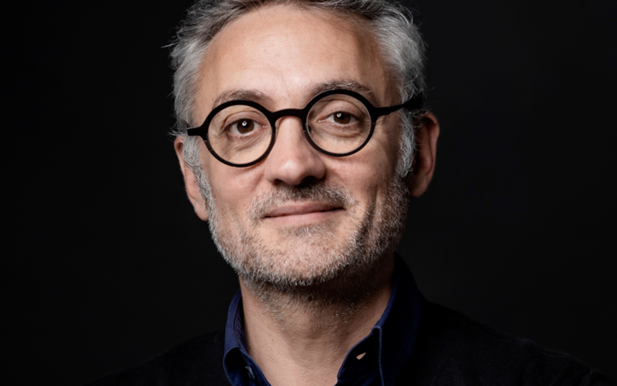 Sur fond noir, un homme pose avec des lunettes rondes