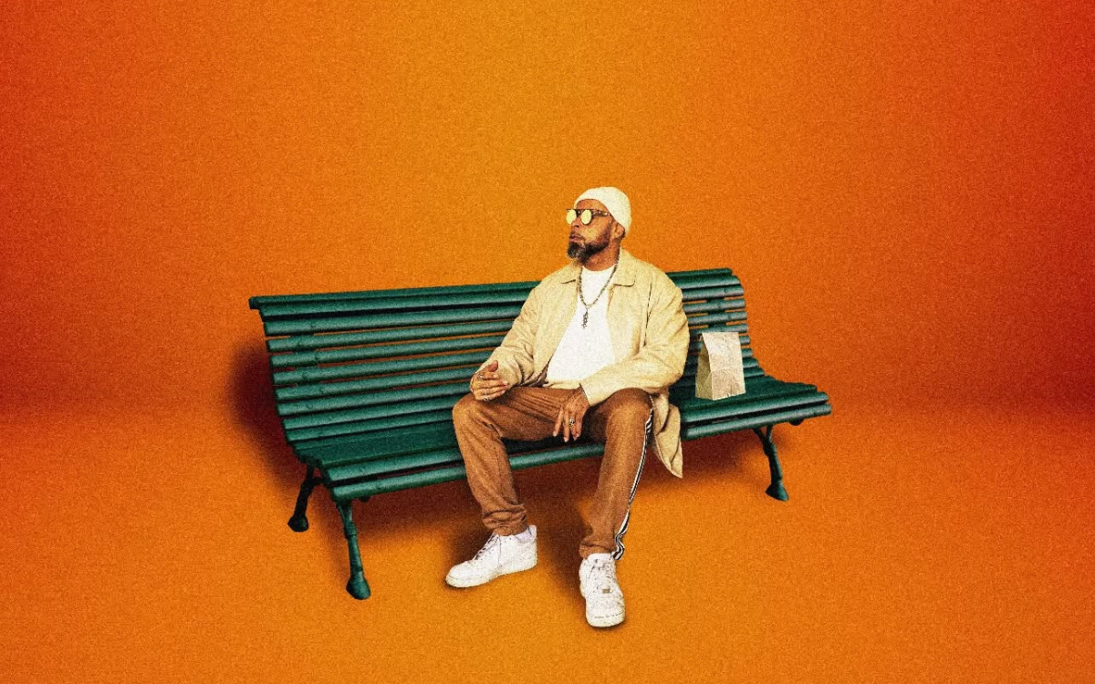 L'artiste Rocé sur fond orange assis sur un banc public
