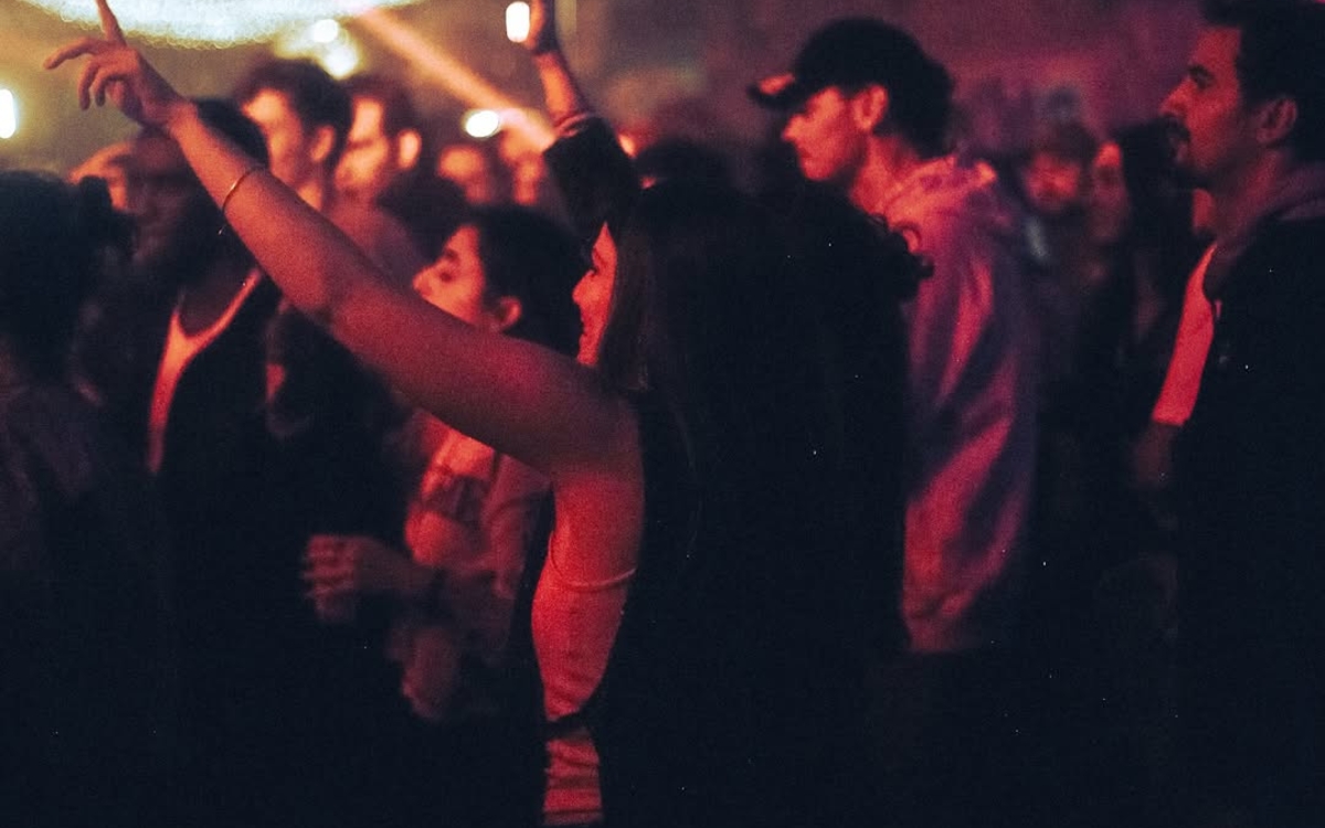 Dans un club, une femme au milieu d'une foule danse les bras levés