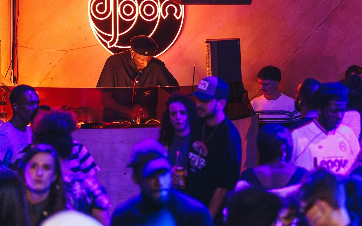 Premier plan, personnes dansent, second plan, un homme derrière des platines