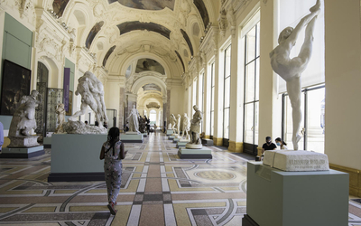 Une femme de dos déambule à l'intérieur du Petit Palais au milieu des sculptures
