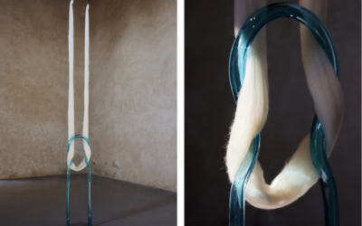 Une installation artistique contemporaine montrant une structure en verre bleu transparent en forme de boucle verticale. Deux longues mèches de fibres blanches (ressemblant à de la laine ou du coton) passent à travers la boucle et tombent jusqu'au sol. L’image de gauche montre l’installation entière dans une pièce aux murs en plâtre beige, tandis que l’image de droite offre un gros plan sur la texture des fibres et la transparence du verre.