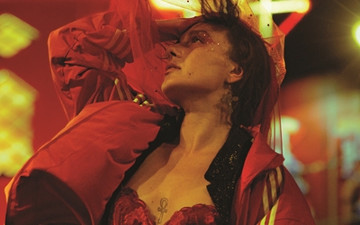 Une danseuse en veste et tenue de sport rouge, dans un environnement lumineux rouge et jaune, prend la pose fièrement