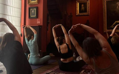 Plusieurs femmes de dos sur un tapis de yoga au milieu de tableaux