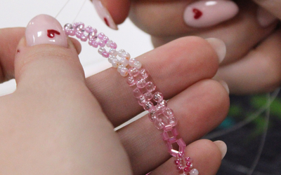 Photographie de mains tenant un bracelet rose conçus en perles de rocaille.