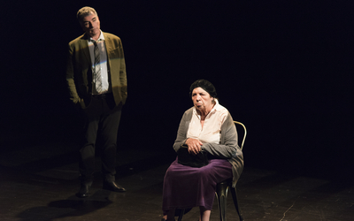 Sur une scène de théâtre, une vieille dame assise, un homme derrière la regarde